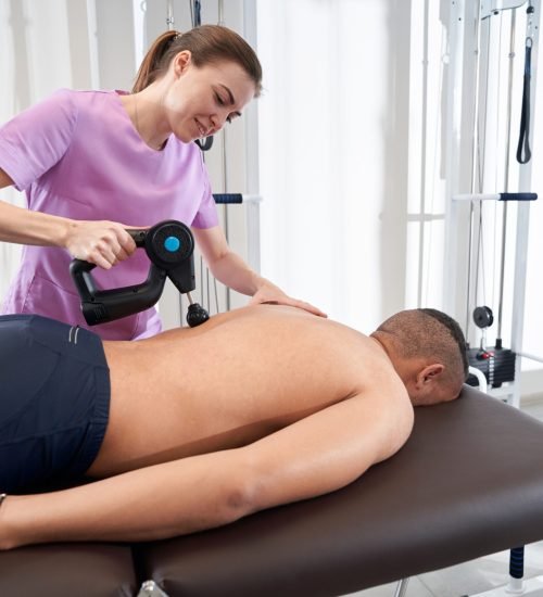 Smiling woman doctor massaging male back with physiotherapy vibration massage device
