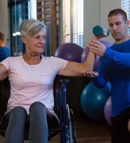 Male physiotherapist helping patient in performing exercise with dumbbell in clinic