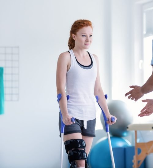 Woman with crutches during rehabilitation with helpful physiotherapist